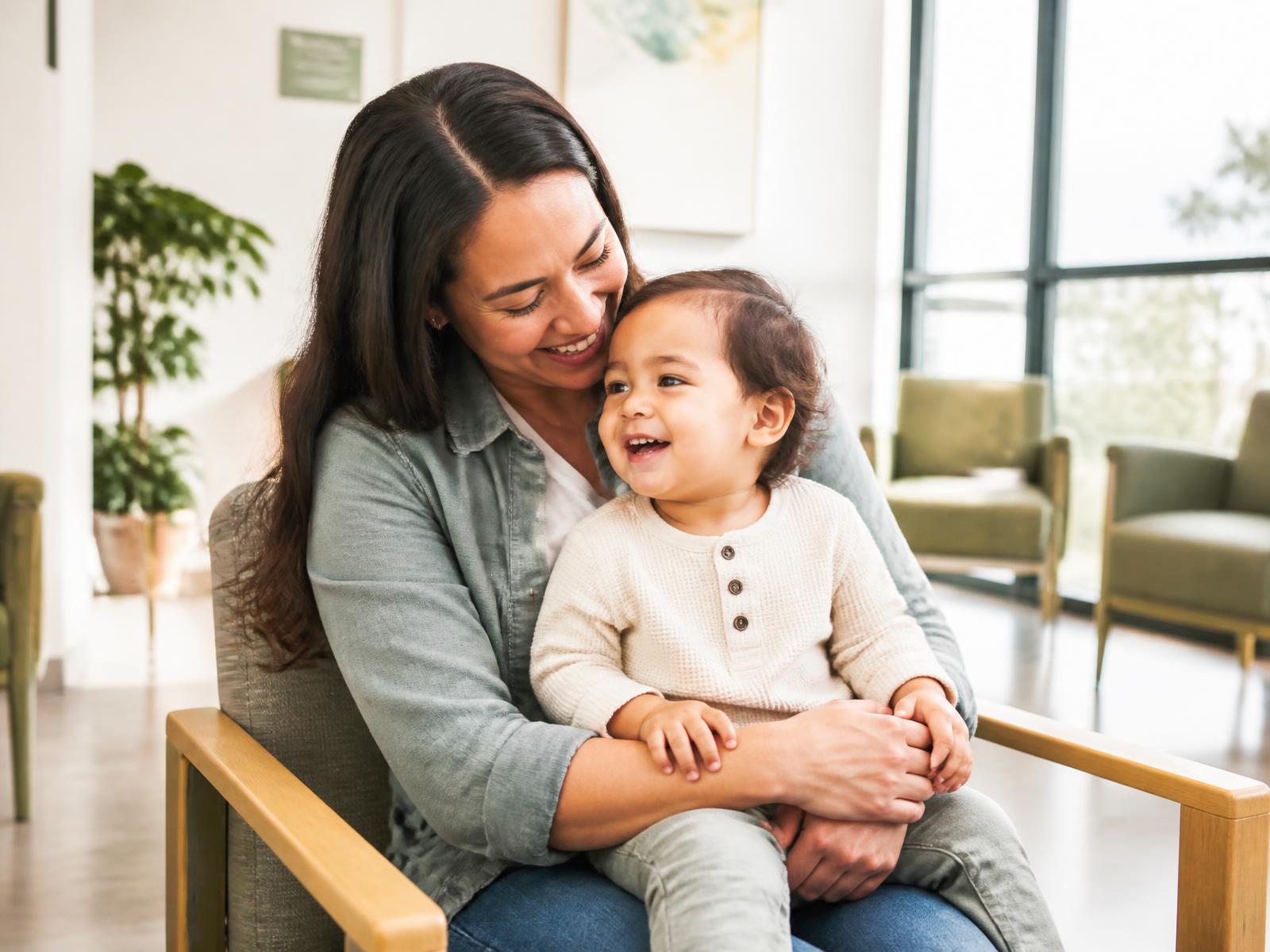 A mother holding her smiling toddler in a bright, calm waiting area